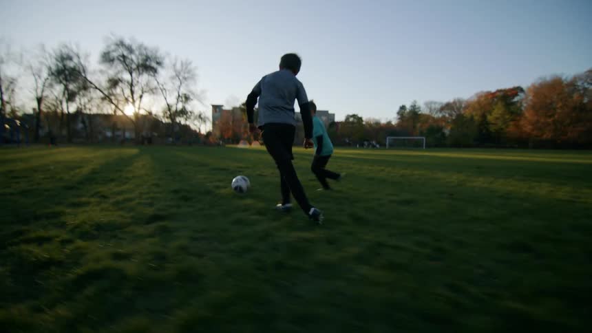 Boys playing football on a grassy field in the morning