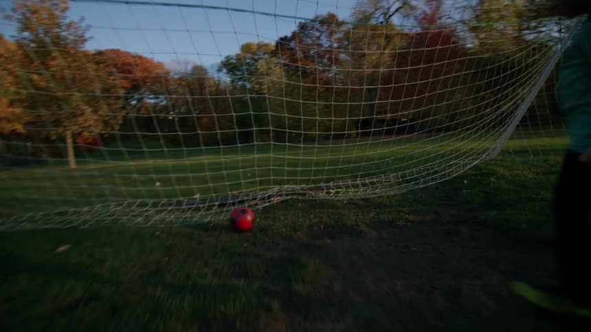 Boy kicking the ball into the goal and then grabbing it with his hands running again