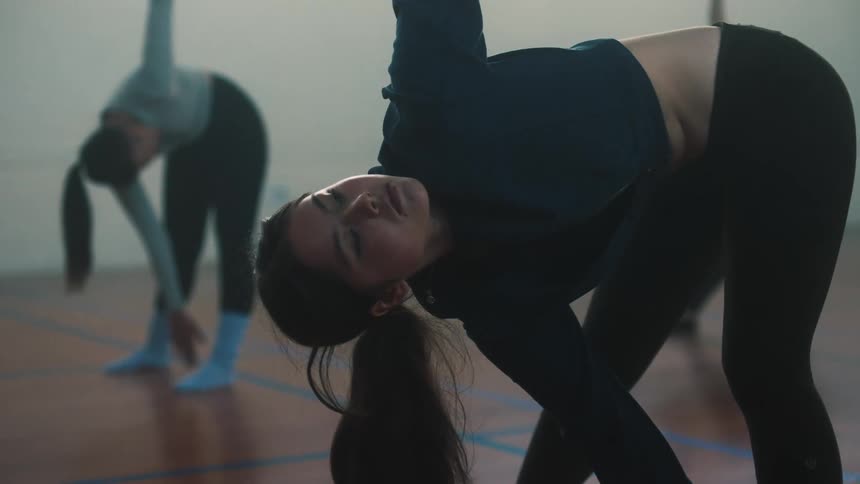 Two females stretching arms indoor while in a bent position