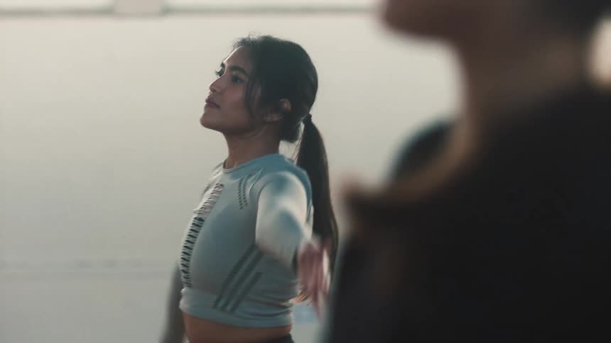 Two women do arm stretches while standing in a gym