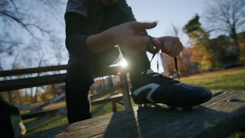 Boy sitting on a bench in the park ties soccer shoes