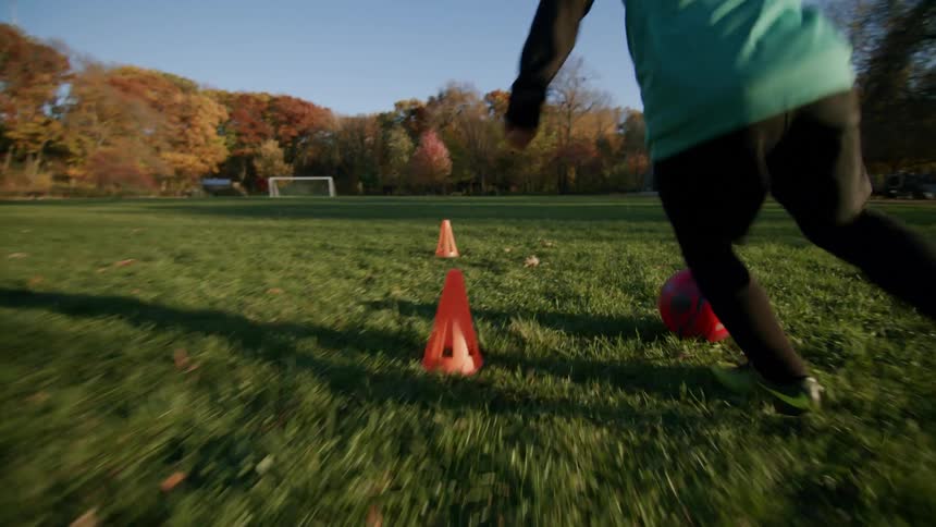 A boy playing soccer ball around cones during the day