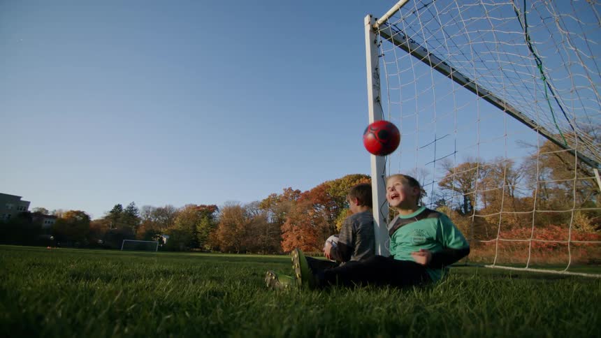 Two boys sitting by the goal play with soccer balls on the soccer field