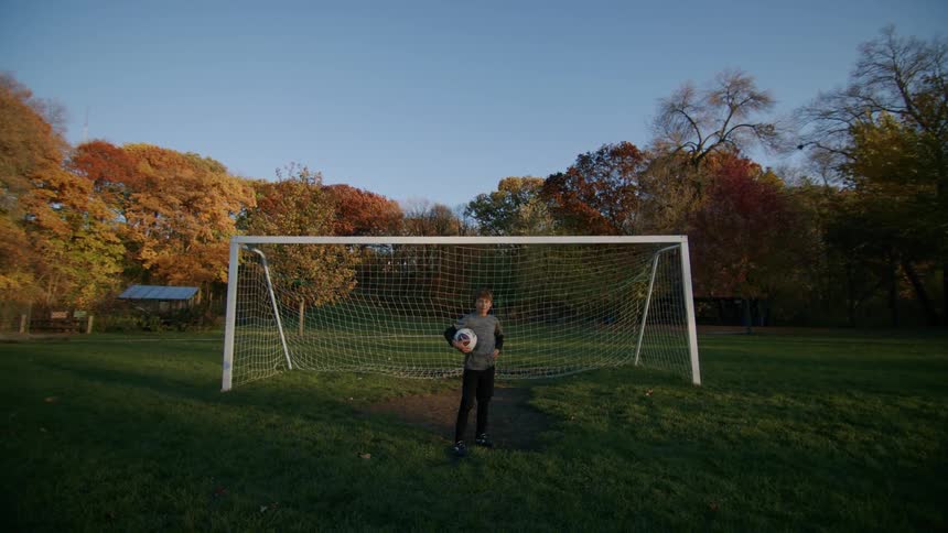 A boy holds a soccer ball striking a pose in front of the goal on the soccer field