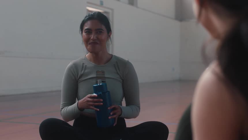 Female friends sitting on a court chatting with one of them having a drink