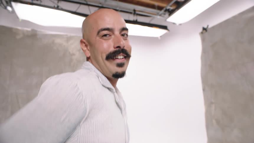 A bald man with a mustache wearing jeans is smiling white cyc levi jeans photography