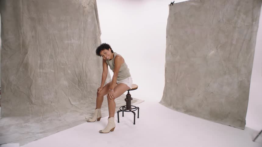 Woman modeling on a white background with a light look and ankle boots dancing sitting on chair white cyc studio