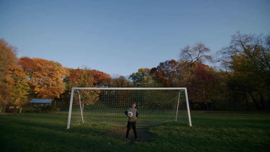 Young goalie stands in front of a soccer goal at morning