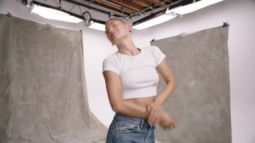 A woman is standing and doing a solo dance wearing a white shirt and jeans