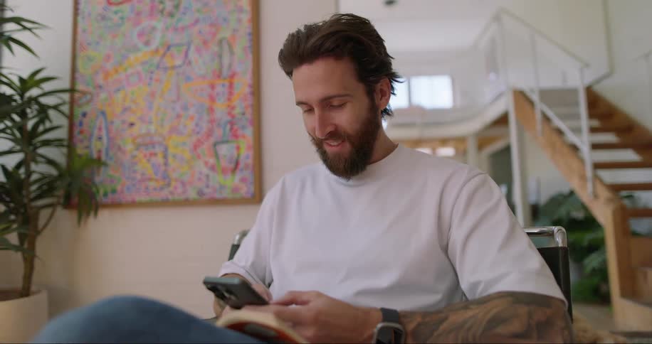 A man is sitting and looks at his cell phone and starts typing