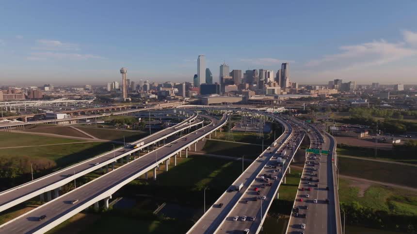 This aerial image shows a busy highway intersection with a city skyline in the background