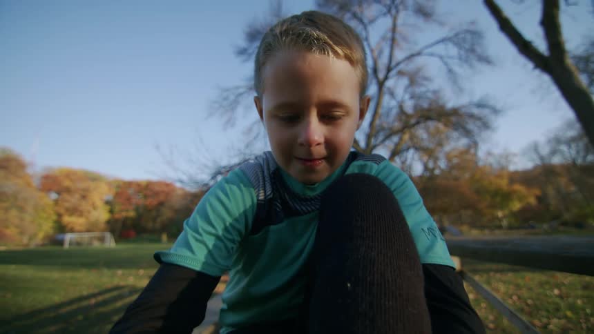 Portrait of a boy with his feet on a bench tying the laces of his soccer cleats