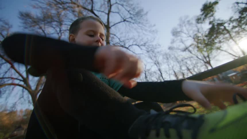 A young boy ties his shoelaces while sitting on a bench on an autumn day