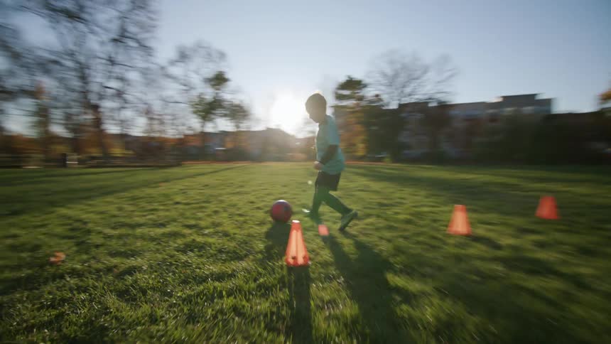 A boy playing soccer ball around cones on a grass field during the day