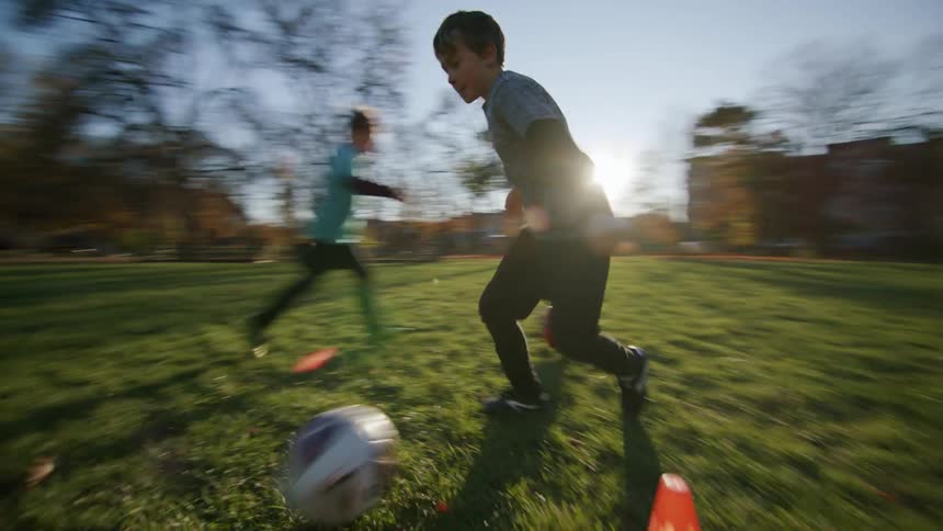 Two boys carrying out football training between the cones one morning