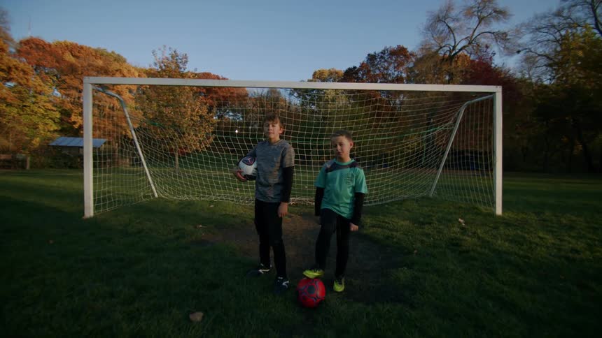 Two young boys stand still in front of a soccer net on a clear autumn day
