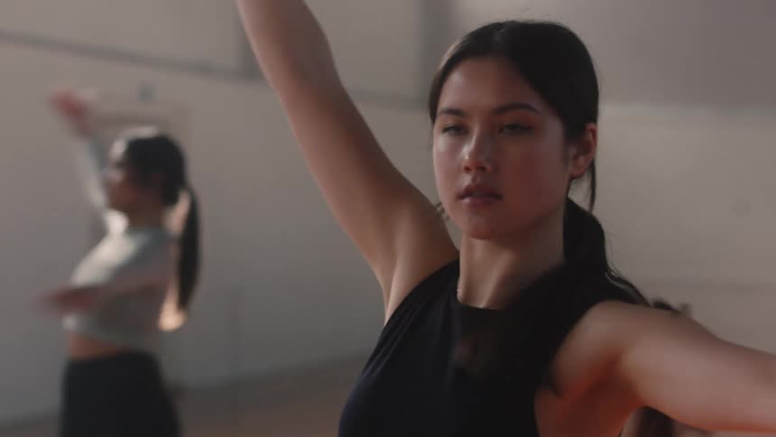 Portrait of a young woman spinning her body in a ballet movement inside an indoor hall with other people