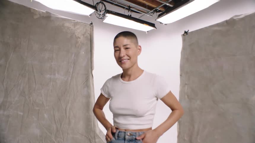 An asian woman with short hair is smiling while sitting on a stool in a photo studio geting ready for a photo shoot whip pan transition