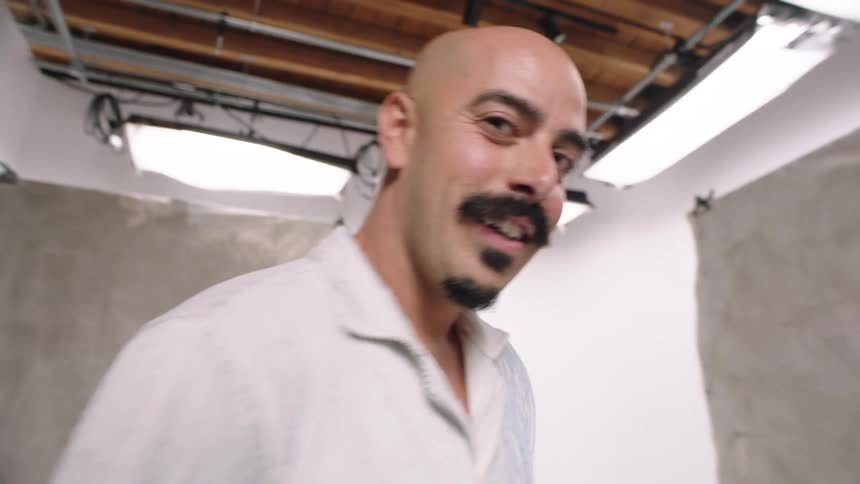 A bald man models denim jeans in a tiny room with a gray backdrop white cyc photo photography backdrop