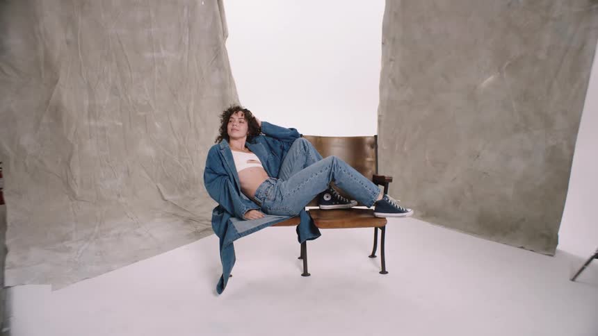 A female sitting on a bench looking happy while wearing jeans clothing woman dancing sitting on chair denim studio photoshoot white cyc