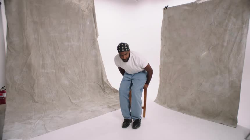 Man grabbing a chair and sitting in the center of a white cyc studio modeling with arms crossed blue collar denim levi wrangler