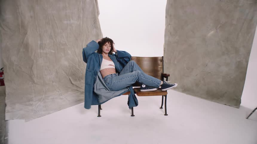 Woman sitting in a chair modeling with a coat and jeans female dancing denim white cyc studio photoshoot