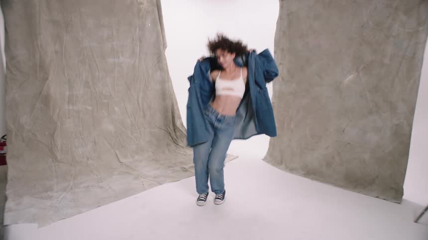 Woman with curly hair a blue overcoat and jeans dances in front of backdrops in the white cyc studio woman dancing denim