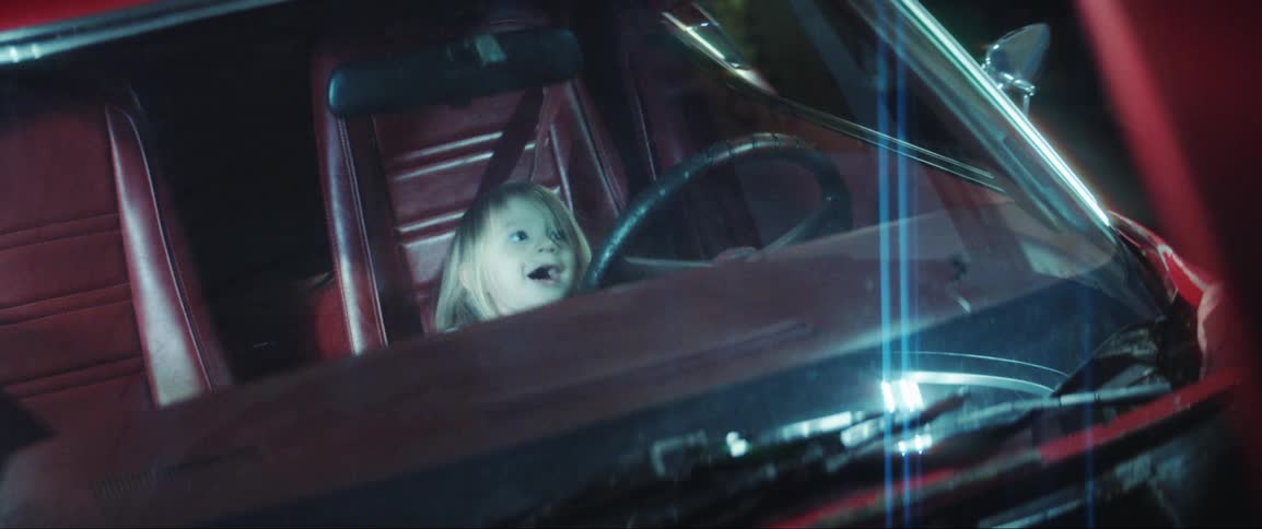 Father checking the vehicles engine while his daughter sits in the front seat of the car in a garage