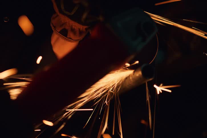 A young boy is cutting an object using a tool and it is making lots of sparks