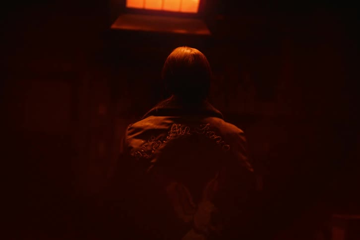 Woman from behind putting on a jacket inside a dark room