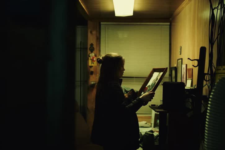 Portrait of a young woman picking up a frame with photos and feeling emotional