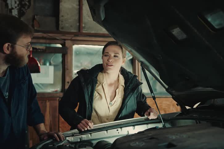 Woman talking next to a man observing the engine of a vehicle in a workshop