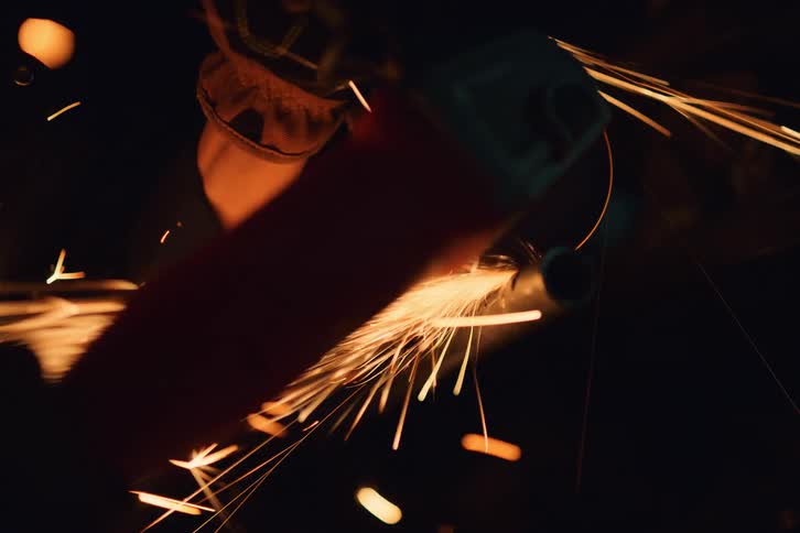 Portrait of a young woman with protective glasses using a cutting machine that emits sparks