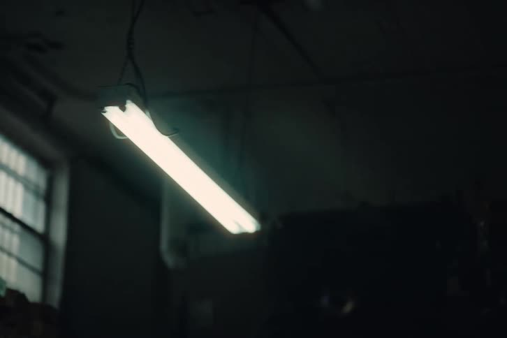 Fluorescent lights hang from the ceiling in a storage room with white boxes on shelves