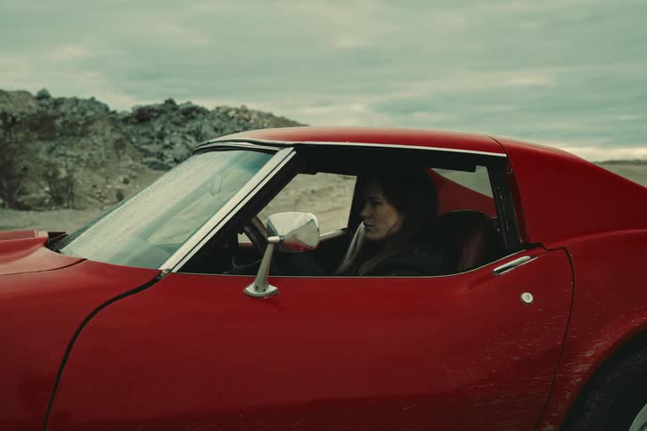 A red chevrolet corvette drives down a dirt road