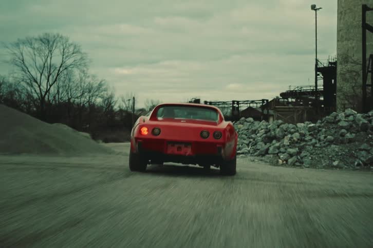 A red chevrolet corvette c3 is driving down a dirt road