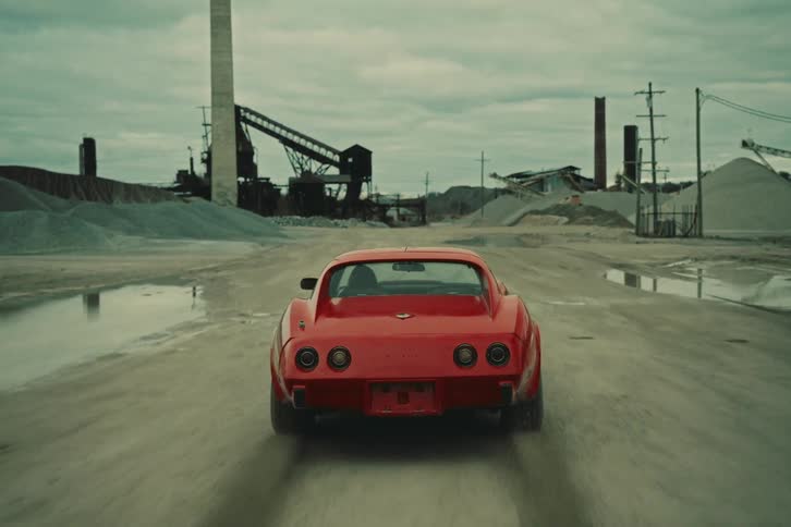 View of an old red sports car being driven through a construction site