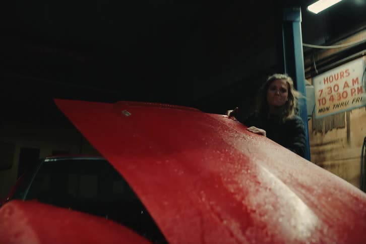 A woman opening a hood of a red car in a garage