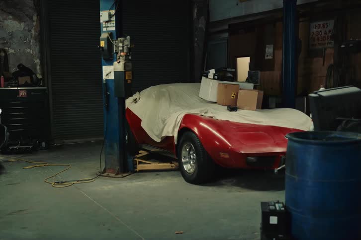Woman from the back looking at a red coupe vehicle abandoned in a garage