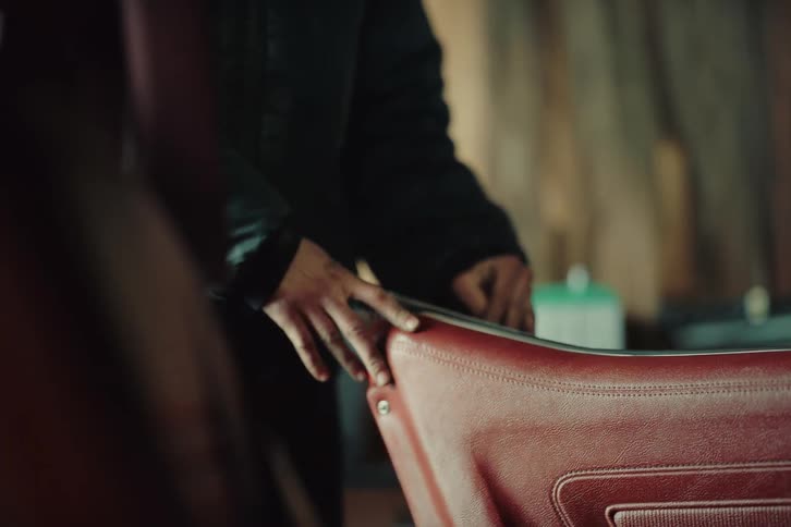 A woman wearing a jacket gets into a car in a garage during the day