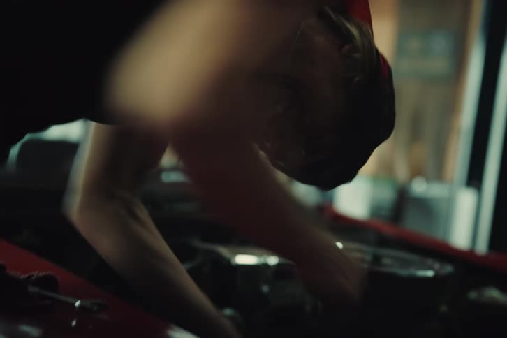 A woman walks up to a car engine with an open hood to fix something and gets nervous and throws the tool that was in her hand on the ground