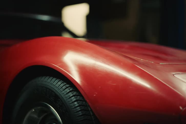A red car with dust on its battery is in a garage