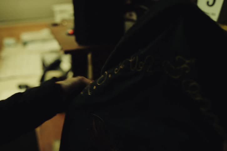A woman walks into an office and looks at an embroidered jacket hanging on a coat rack touching it fondly