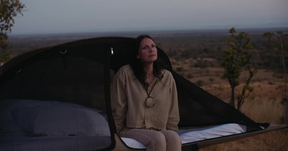 A woman camping in a savanna field at dusk