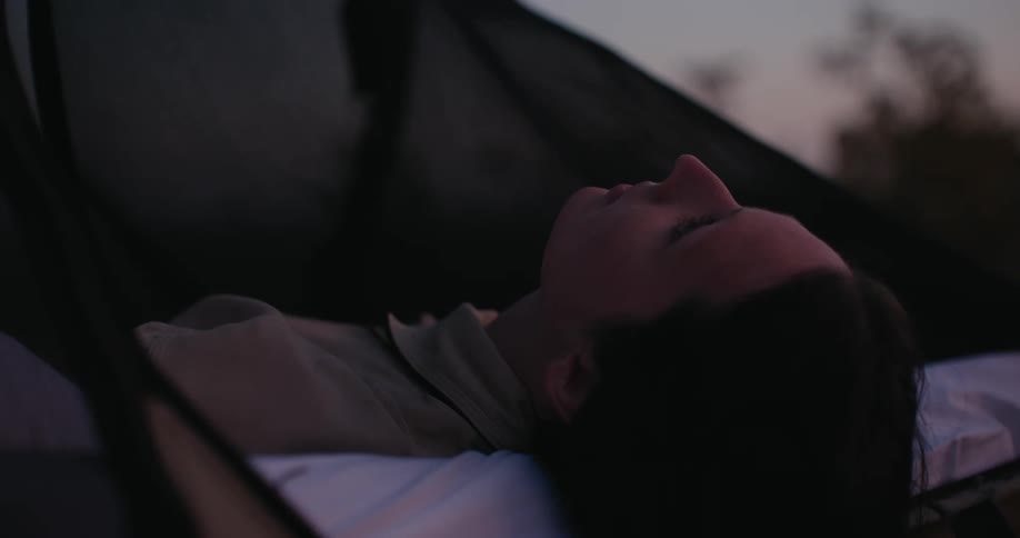 Woman laying on her back in a hammock looking at the sky at dusk or dawn
