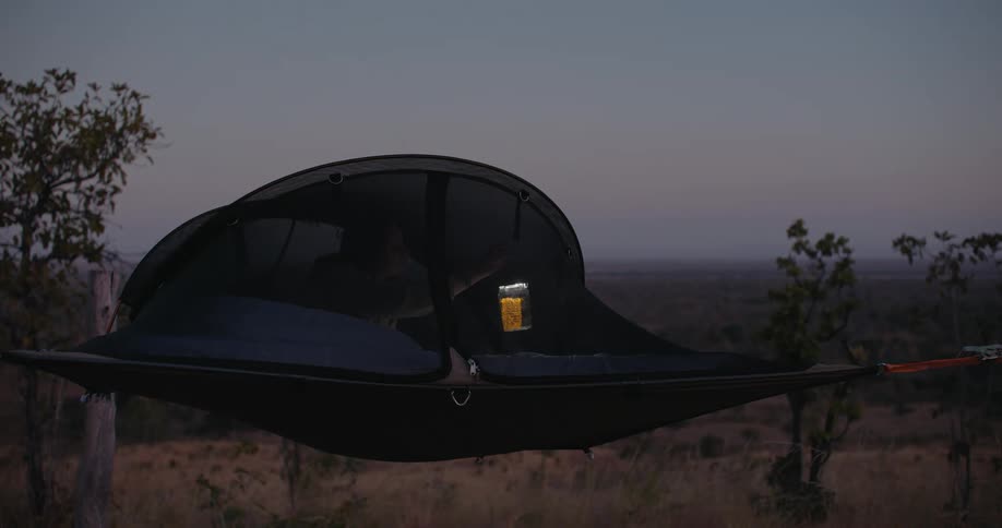 Camper relocates hanging lantern inside tent and lies down