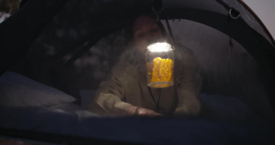 A woman hangs a lantern in her tent and goes to sleep