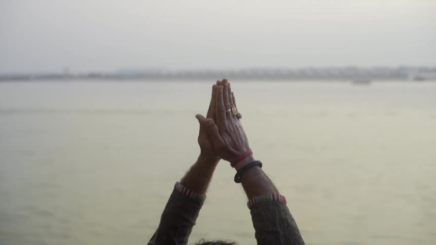 Hands of a person with palms pressed together facing the sea