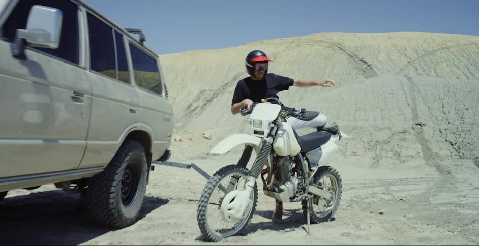 Man wears a helmet and gets on a dirt bike in the desert