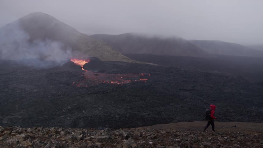 Hiker moves across plain while smoke rises from erupting volcano in the background